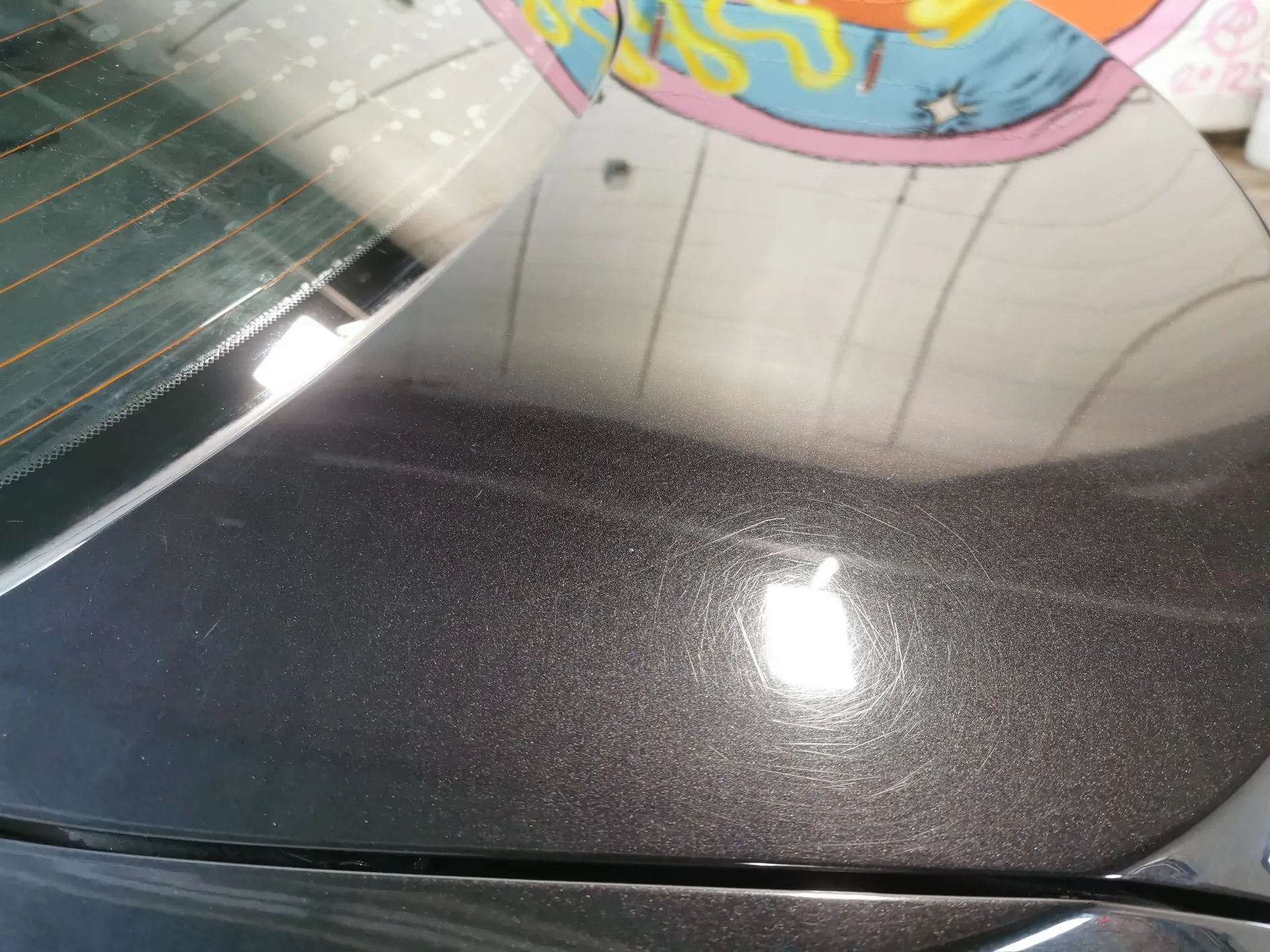 Macro of dark metallic paint showing fine scratches and marring under bay lighting, before professional paint correction